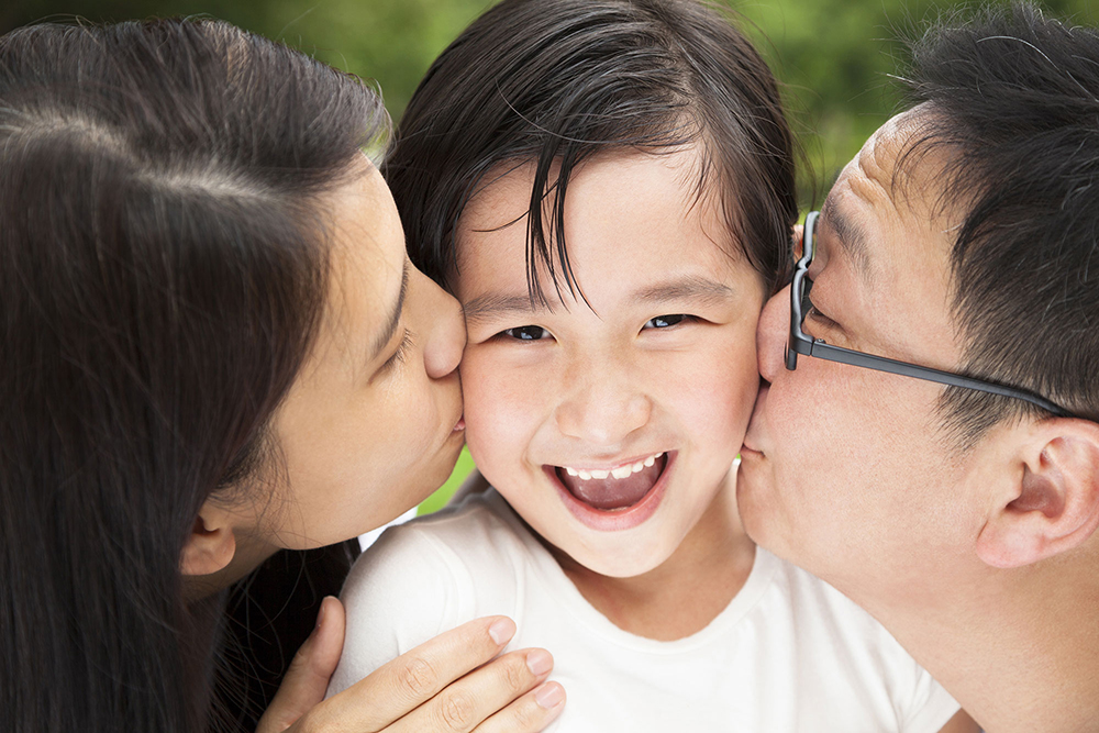 parents kissing smiling son's cheeks image